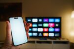 Smart-TV mit App-Übersicht im Wohnzimmer, davor ein Smartphone