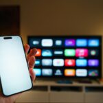 Smart-TV mit App-Übersicht im Wohnzimmer, davor ein Smartphone