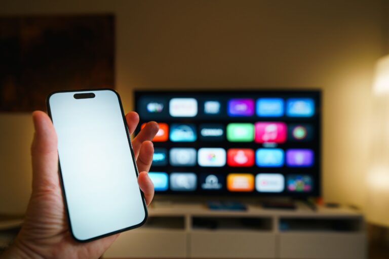 Smart-TV mit App-Übersicht im Wohnzimmer, davor ein Smartphone