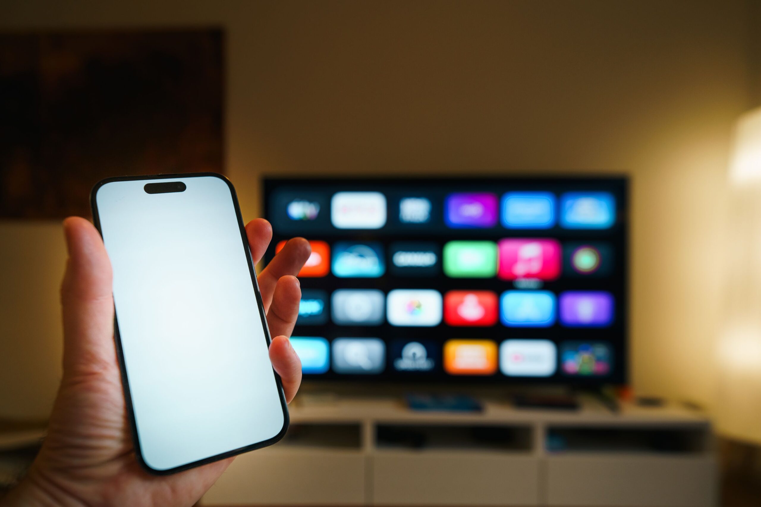 Smart-TV mit App-Übersicht im Wohnzimmer, davor ein Smartphone